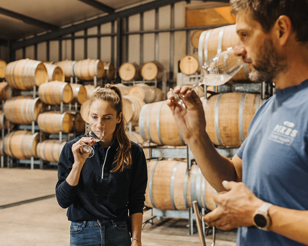 Two people tasting wine in a winery with barrels in the background