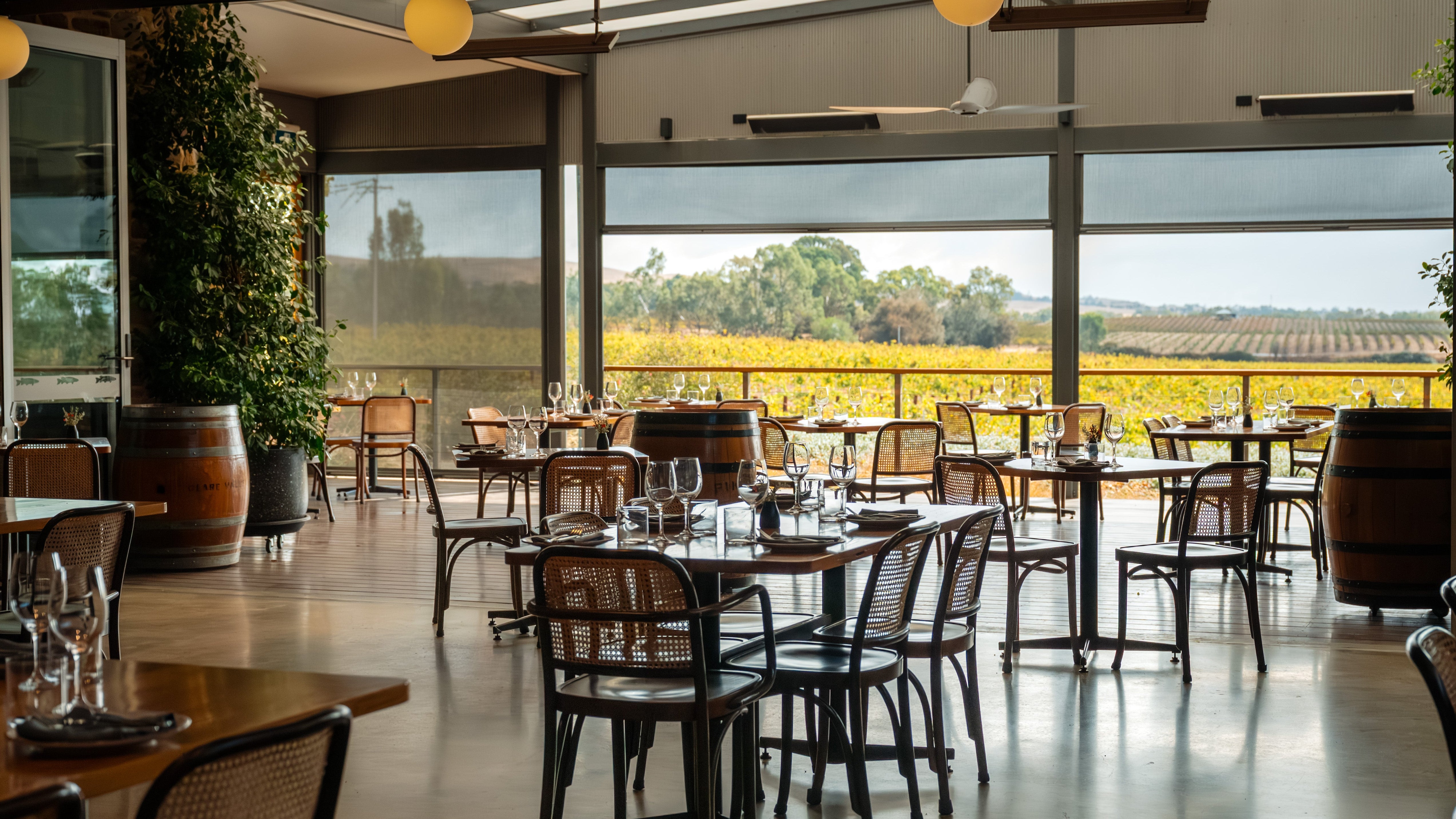 Modern restaurant interior with tables and chairs overlooking a scenic view of a field.