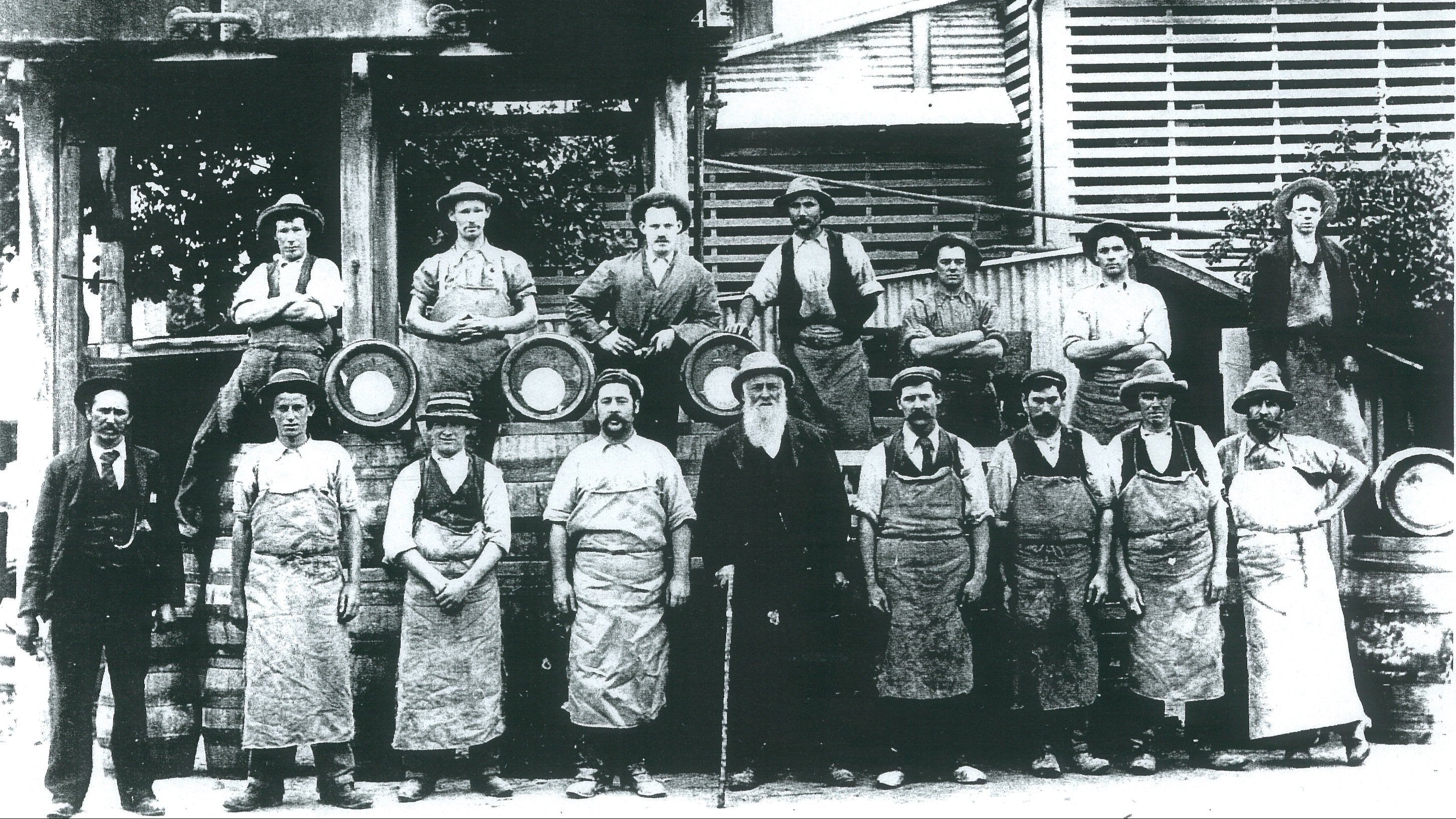 Black and white photograph of a group of men in aprons standing in front of a building with barrels.