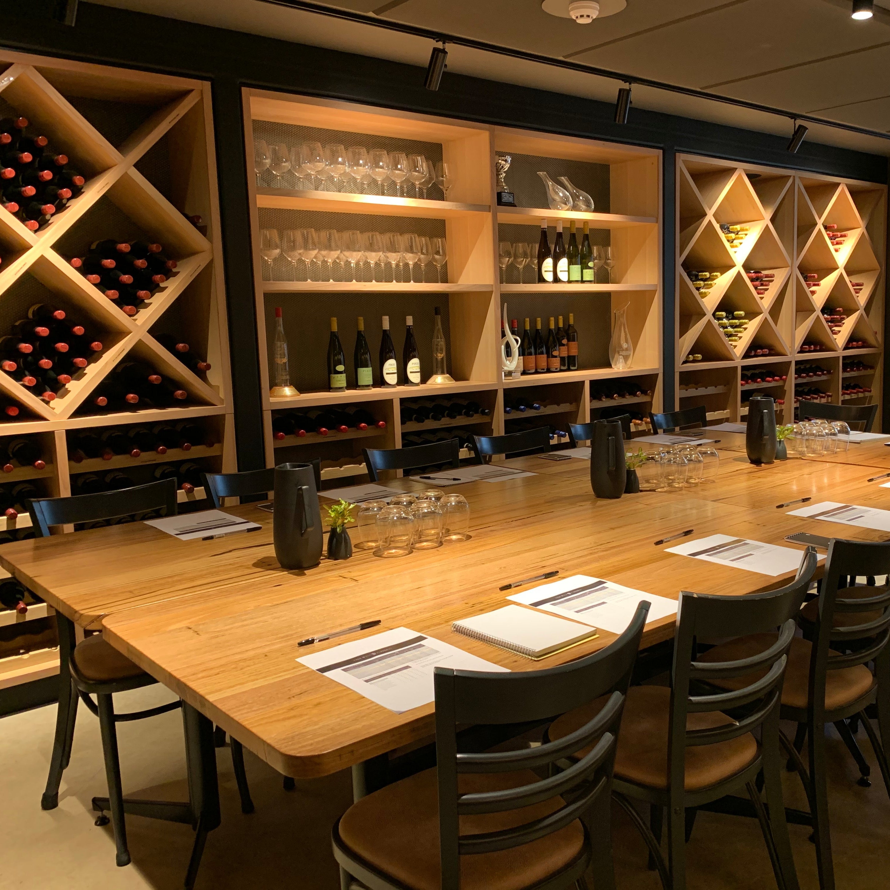 Modern wine cellar with wooden table and chairs, wine bottles, and glasses.